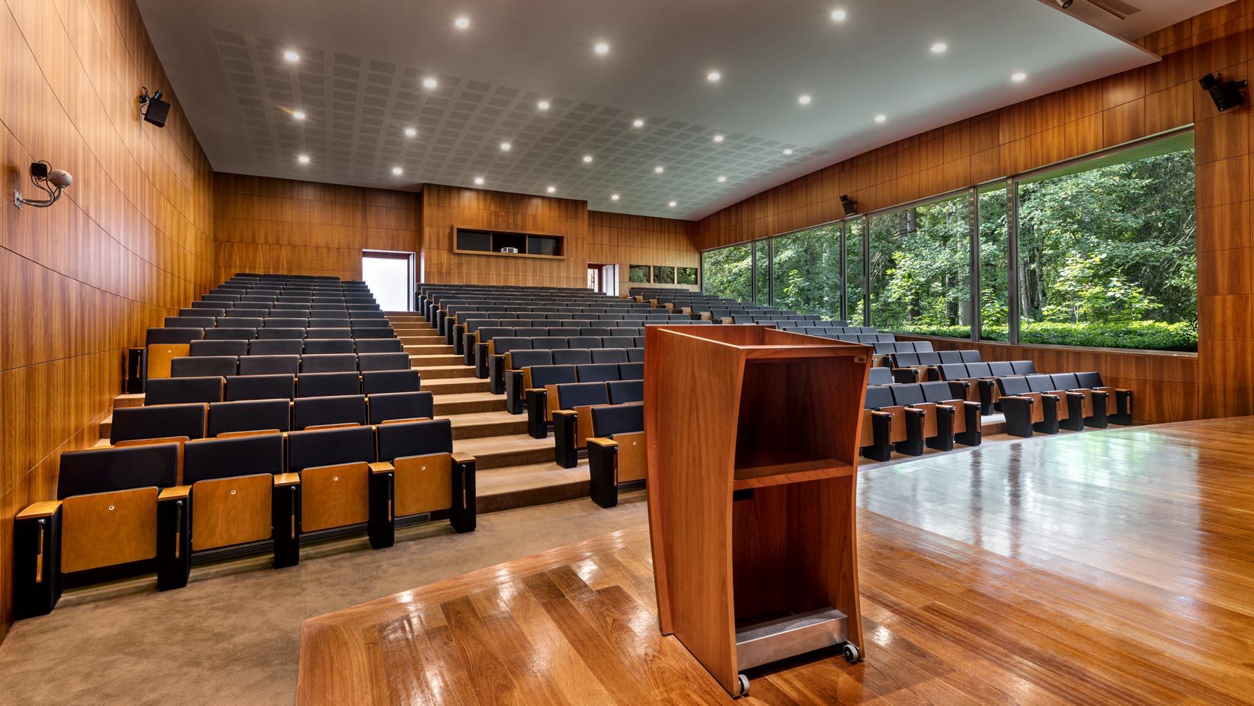 Lichte, moderne collegezaal met houten lambrisering en een leeg spreekgestoelte
